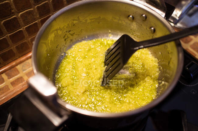 From above of crop unrecognizable chef frying chopped garlic and onion in metal pan while cooking food in kitchen at home — Stock Photo