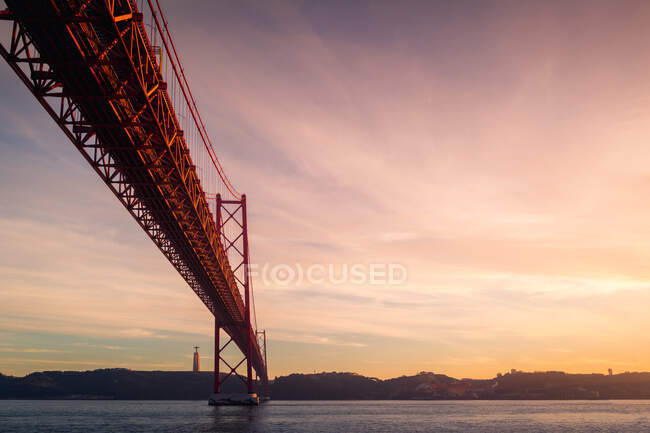 De baixo de postes de amarração de metal enferrujado localizados na margem do rio Tejo sob a Ponte 25 de Abril ao pôr-do-sol em Lisboa, Portugal — Fotografia de Stock