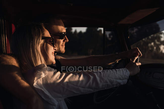 Vista laterale di coppia amorevole in occhiali da sole che abbraccia in auto d'epoca mentre si guida nella natura in serata — Foto stock