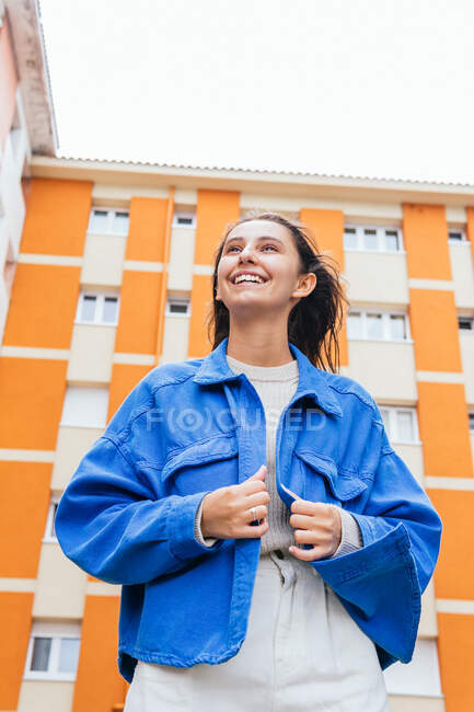 Low angle of cheerful female standing in street against bright building and laughing — Stock Photo