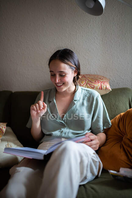 Femme assise sur un canapé dans le salon et lisant un livre — Photo de stock