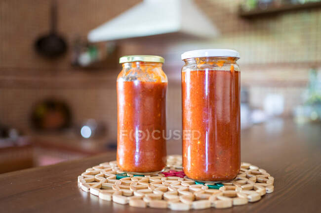 Sabrosa salsa marinara casera de tomates en frascos de vidrio colocados en la mesa de madera en la cocina - foto de stock