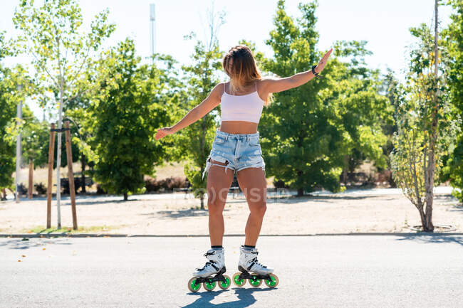 Joven hembra en patines que muestra acrobacias en carretera en la ciudad en verano - foto de stock