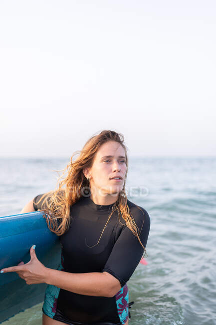 Weibchen im Badeanzug stehen im Sommer mit SUP-Board im Meerwasser und schauen weg — Stockfoto
