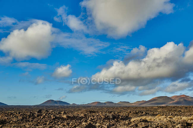 Nuvens brancas flutuando no céu azul sobre colinas e vale coberto com pedras no dia ensolarado de verão em Fuerteventura, Espanha — Fotografia de Stock