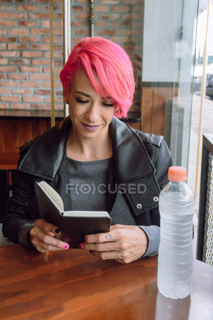 Von oben eine Frau in lässiger Kleidung, die ein geöffnetes Notizbuch auf einem Holztisch hält — Stockfoto