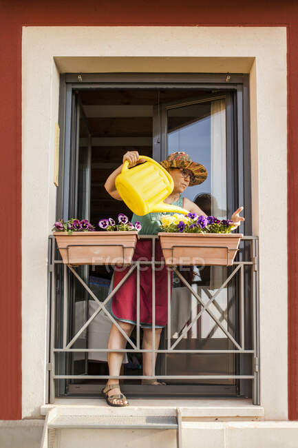Von unten gießt eine reife Gärtnerin die Pflanzen des Balkons ihres Hauses — Stockfoto