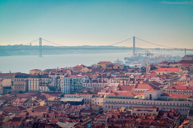 Vista del dron de edificios techados rojos ubicados en la costa del río Tajo no lejos del puente 25 de Abril en la mañana en Lisboa, Portugal - foto de stock