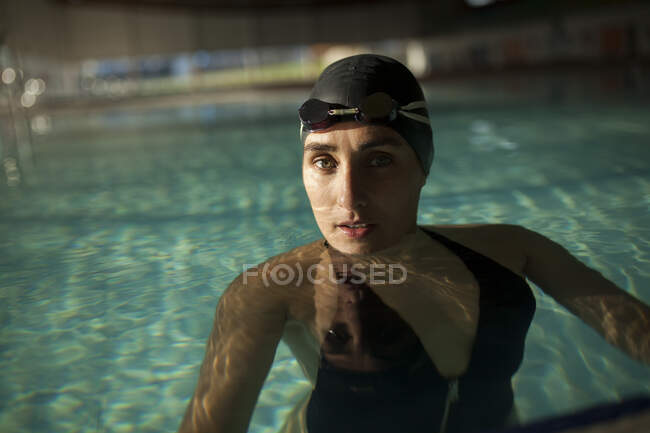 Jeune belle femme dans la piscine intérieure, portant un maillot de bain noir, regardez la caméra — Photo de stock