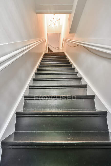 From below perspective view of stairway with black steps and white railings leading to upper floor with glowing chandelier in residential house — Stock Photo