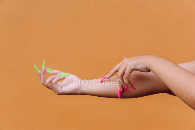 Crop anonymous female with manicured long nails gently touching hand skin against orange background — Stock Photo