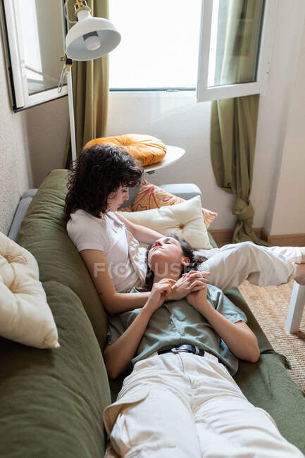 Zarte lesbische Frau auf Knien liegend von liebenden Freundin, die zu Hause auf der Couch sitzt und sich am Wochenende entspannt — Stockfoto