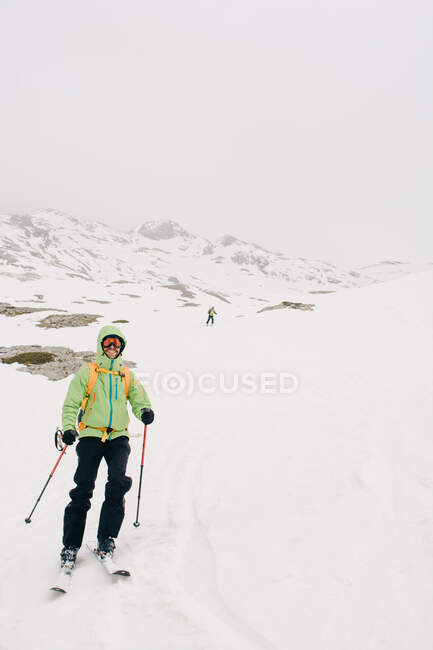 Alegre deportista esquiando sobre nieve con un amigo irreconocible en Pico AunAmendi en Pirineos Montañas en Navarra España - foto de stock