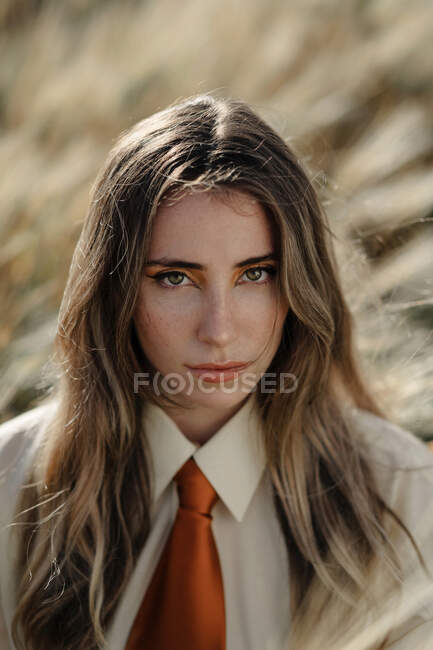 Jeune femme consciente en tenue formelle avec cravate regardant la caméra parmi les pointes dans la campagne — Photo de stock