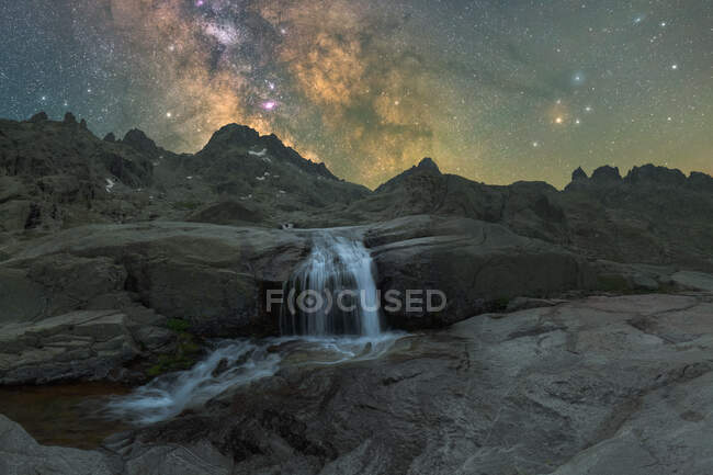 Вчорашнє видовище високих грубих гір з каскадом і річкою під зоряним небом з галактикою. — стокове фото