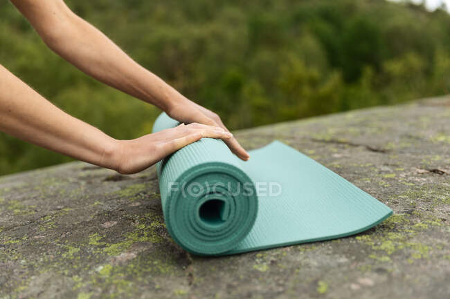 Donna anonima svolgersi stuoia sulla roccia all'inizio della sessione di yoga vicino palude in natura — Foto stock