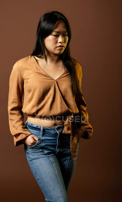 Vue de face de la femelle asiatique en vêtements à la mode regardant vers le bas sur fond brun en studio — Photo de stock