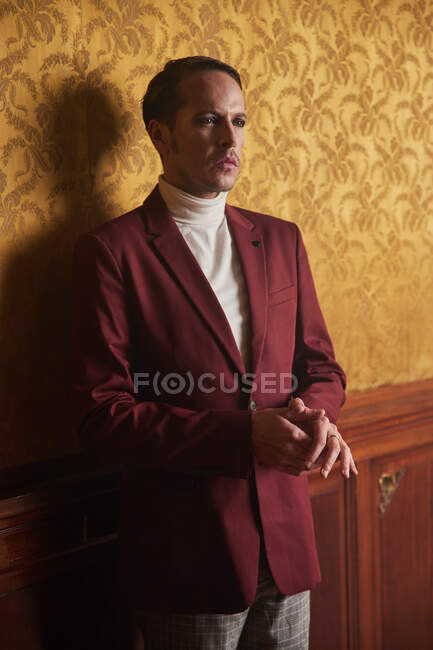 Впевнений дорослий чоловік-актор в елегантному стильному одязі, задумливо дивлячись, стоячи біля стіни в старовинному стилі кімнати — стокове фото
