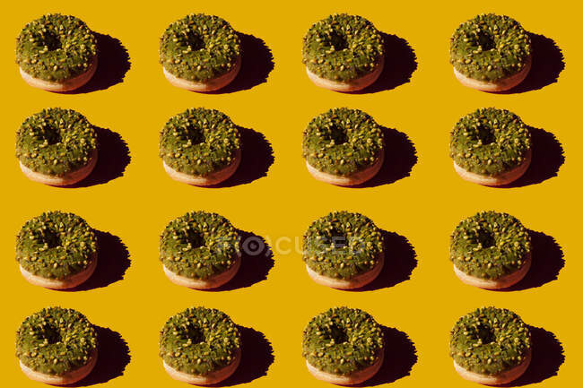 De arriba muchas rosquillas cubiertas con la cubierta verde y las nueces sobre el fondo amarillo - foto de stock