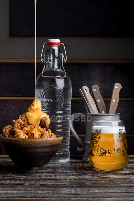 Served table with bowl with tasty crispy chicken with cheese sauce placed near glass of beer against bottle of water and utensil in restaurant — Stock Photo
