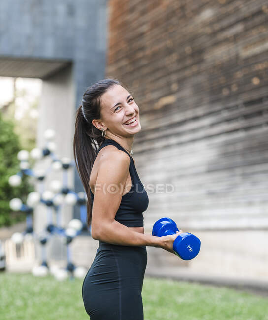 Решительная спортсменка, занимающаяся спортом с гантелями во время тренировки на городской улице летом — стоковое фото