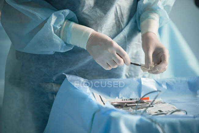 Crop anonymous surgical nurse in disposable gloves disinfecting needle of injector while preparing for surgery in clinic — Stock Photo