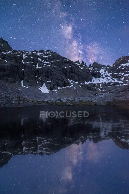Picturesque view of starry sky with galaxy reflecting in lake against mount with snow at dusk — Stock Photo