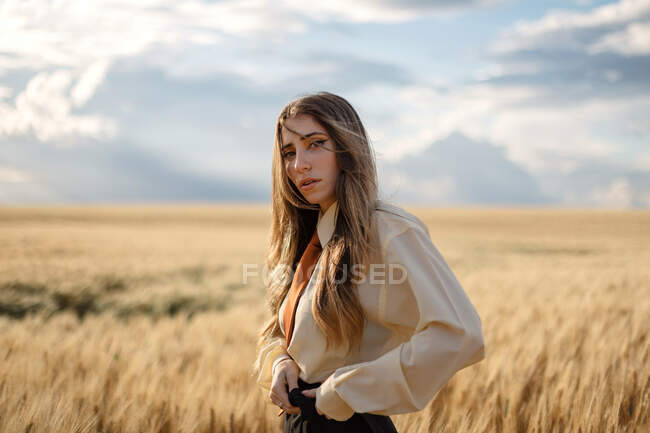 Side view of young mindful female in formal wear with tie looking at camera among spikes in countryside — Stock Photo