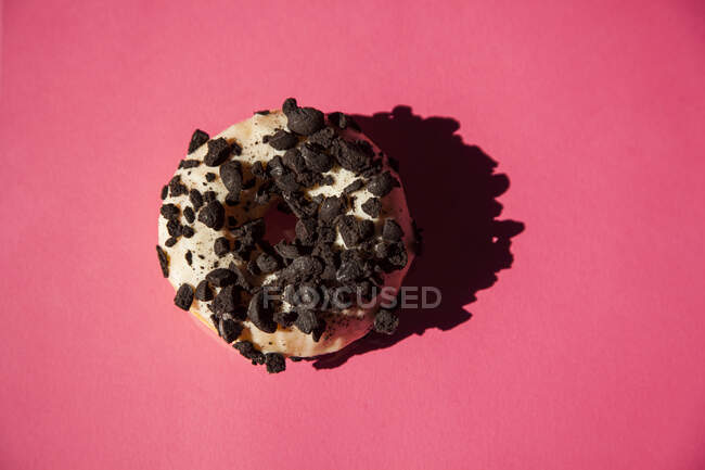 Ciambelle bianche ricoperte oreo pezzi di biscotti al cioccolato su sfondo rosa — Foto stock
