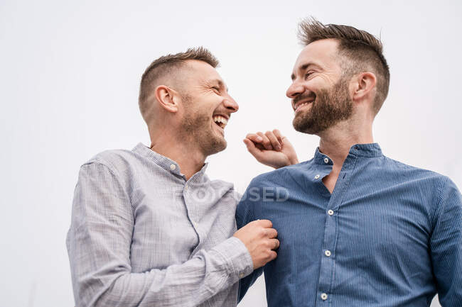 Щасливий чоловік з сучасною зачіскою сміється, розмовляючи з гомосексуальним партнером у сорочці вдень — стокове фото