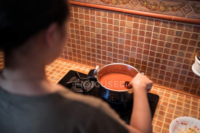 De dessus de la récolte femelle ajoutant du sel dans une casserole pendant la cuisson de la sauce marinara à partir de tomates sur la cuisinière dans la cuisine — Photo de stock