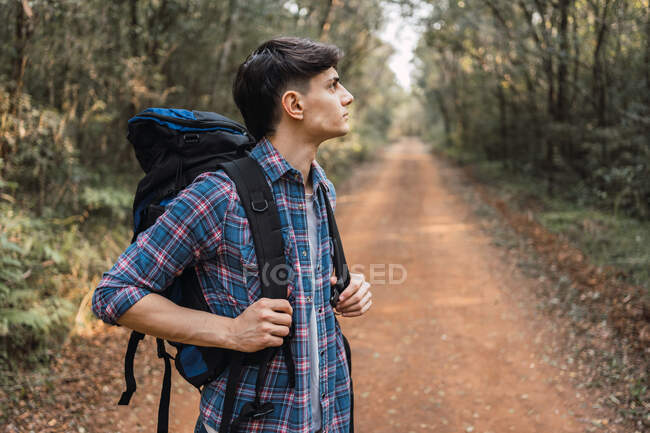 Чоловік-дослідник з рюкзаком, що йде піщаною стежкою в лісі під час походів і озирається — стокове фото