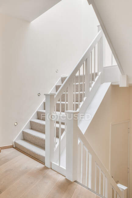 Interior da casa moderna com escadas que levam ao andar superior com corrimão branco e paredes iluminadas com lâmpadas LED modernas em estilo loft minimalista — Fotografia de Stock