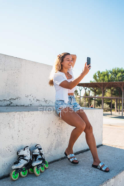 Positivo alegre joven mujer tomando uno mismo disparo en el teléfono móvil en el día soleado en verano en la ciudad - foto de stock