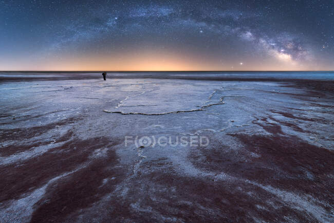 Distant silhouette of explorer photographer taking pictures with camera on a tripod in dry salt lagoon on background of starry sky with glowing Milky Way at night — Stock Photo