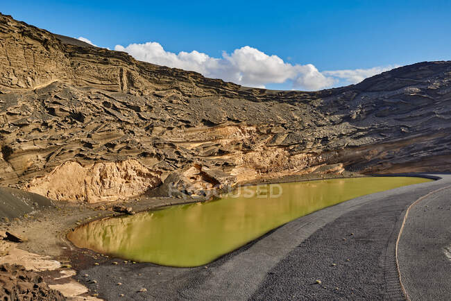 Ruhiger Teich mit gelbem Wasser in der Nähe rauer Steinformationen an einem sonnigen Sommertag auf Fuerteventura, Spanien — Stockfoto