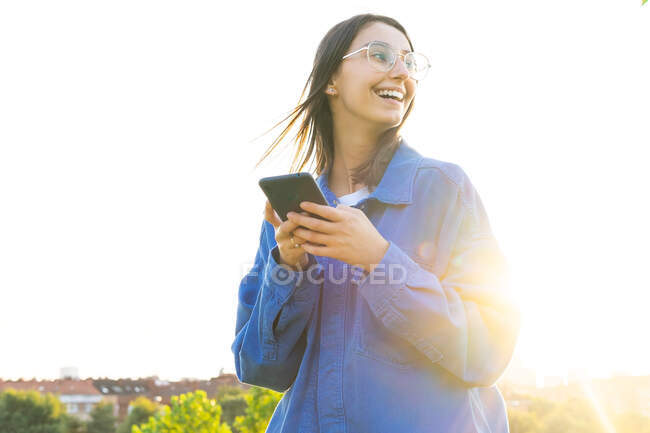 Elegante femmina in piedi su verde collina erbosa e la navigazione su smartphone nella giornata di sole — Foto stock