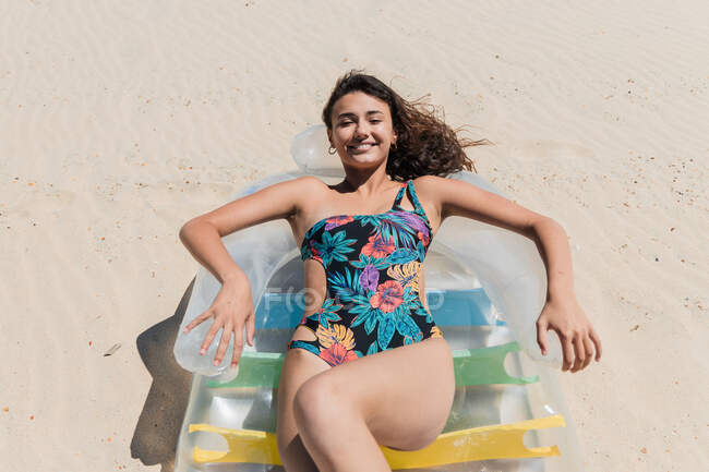 Зверху щаслива жінка в купальнику лежить на надувному матраці на піщаному узбережжі і купається в сонячний день під час літніх канікул — стокове фото