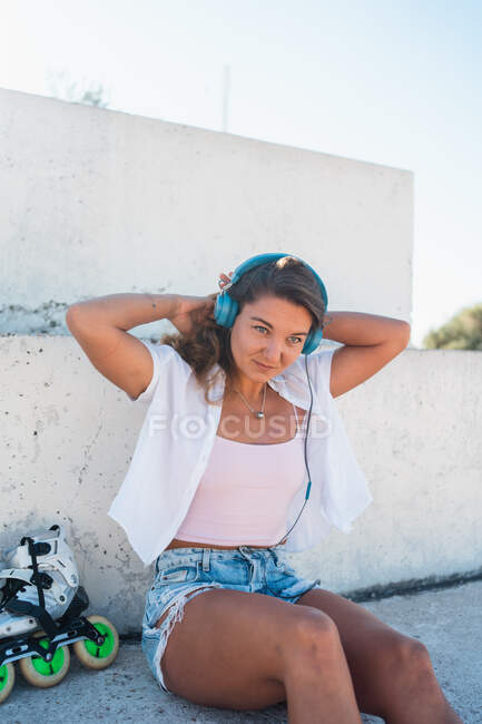 Positive young female listening music on headphones on sunny day in summer in city looking away — Stock Photo