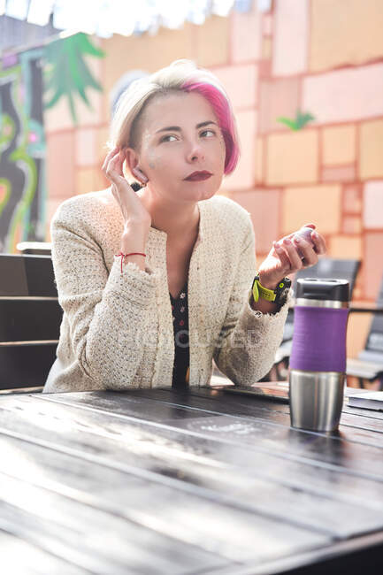 Angle bas de femme alternative heureuse avec cheveux teints prendre le petit déjeuner tout en étant assis à table dans un café de rue et en regardant loin — Photo de stock