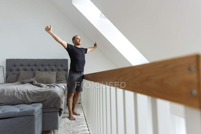 Homme debout près du lit et étirant les bras après le réveil le matin à la maison — Photo de stock