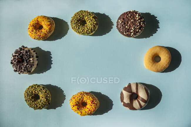 Circle of donuts of different colors and flavors with copy space in the center on blue background — Stock Photo