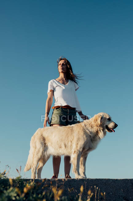 D'en bas jeune femme avec Golden Retriever chien debout sur le rocher et admirant les montagnes à couper le souffle pendant le voyage d'été — Photo de stock