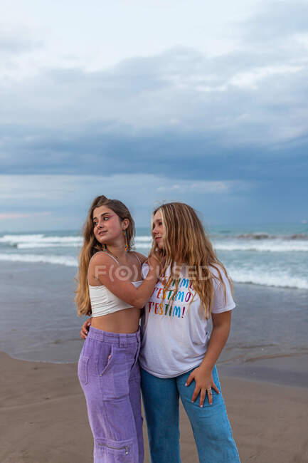 Loving couple of homosexual women hugging while standing on wet seashore in sunset and looking away — Stock Photo