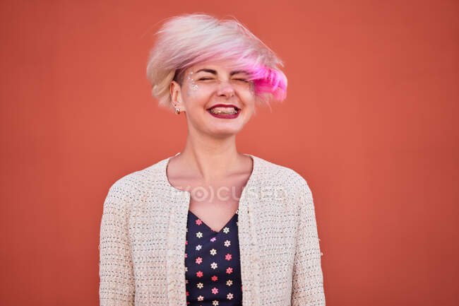 Despreocupado alternativa fêmea jogando cabelo curto tingido contra a parede laranja na área urbana — Fotografia de Stock