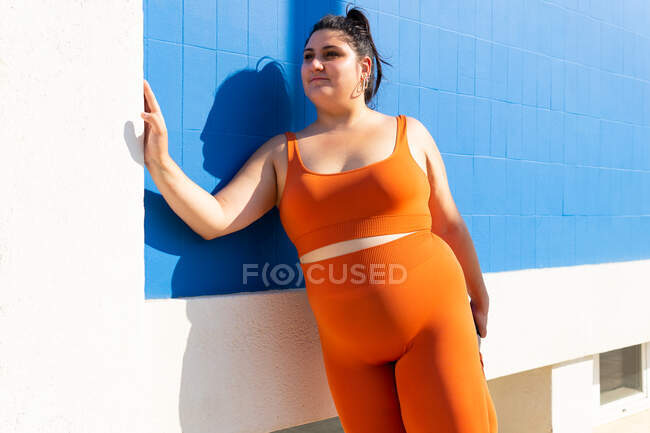 Plump female athlete in sportswear exercising on tiled walkway in sunny town — Stock Photo