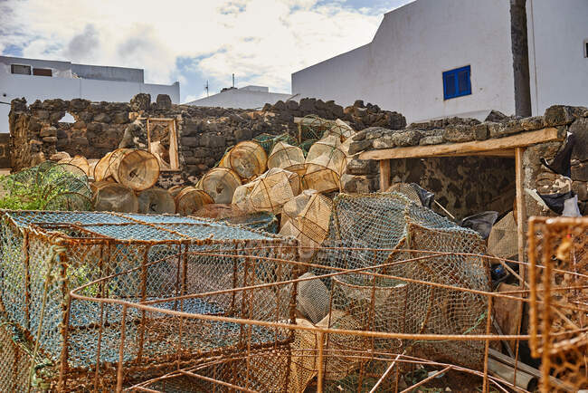 Muchas trampas de peces de varias formas colocadas en el patio cerca de la pared de piedra y casas en el día de verano - foto de stock
