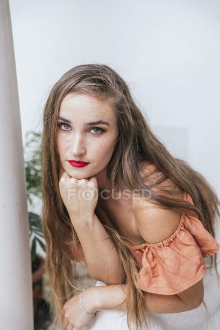 Hohe Winkel der ruhigen Frau mit roten Lippen und langen Haaren lehnt an der Hand beim Chillen auf der Terrasse im Sommer und Blick in die Kamera — Stockfoto