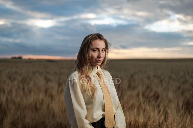 Jovem mindful fêmea em desgaste formal com gravata olhando para a câmera entre picos no campo — Fotografia de Stock