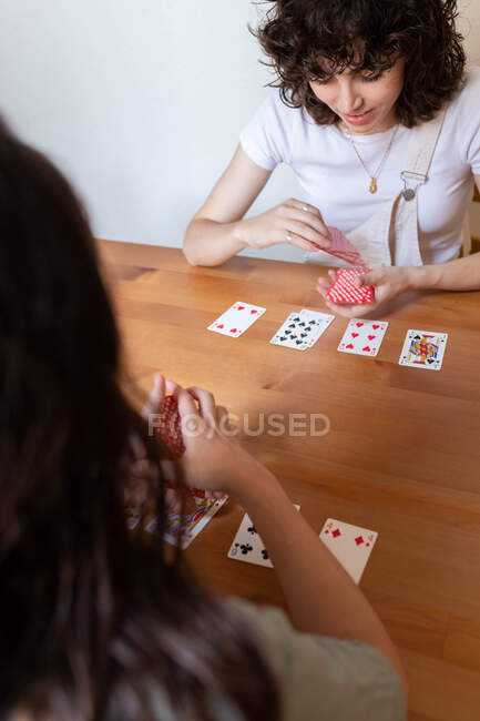 De cima encantado casal LGBT de mulheres sentadas à mesa e jogando cartas enquanto entretendo no fim de semana em casa — Fotografia de Stock
